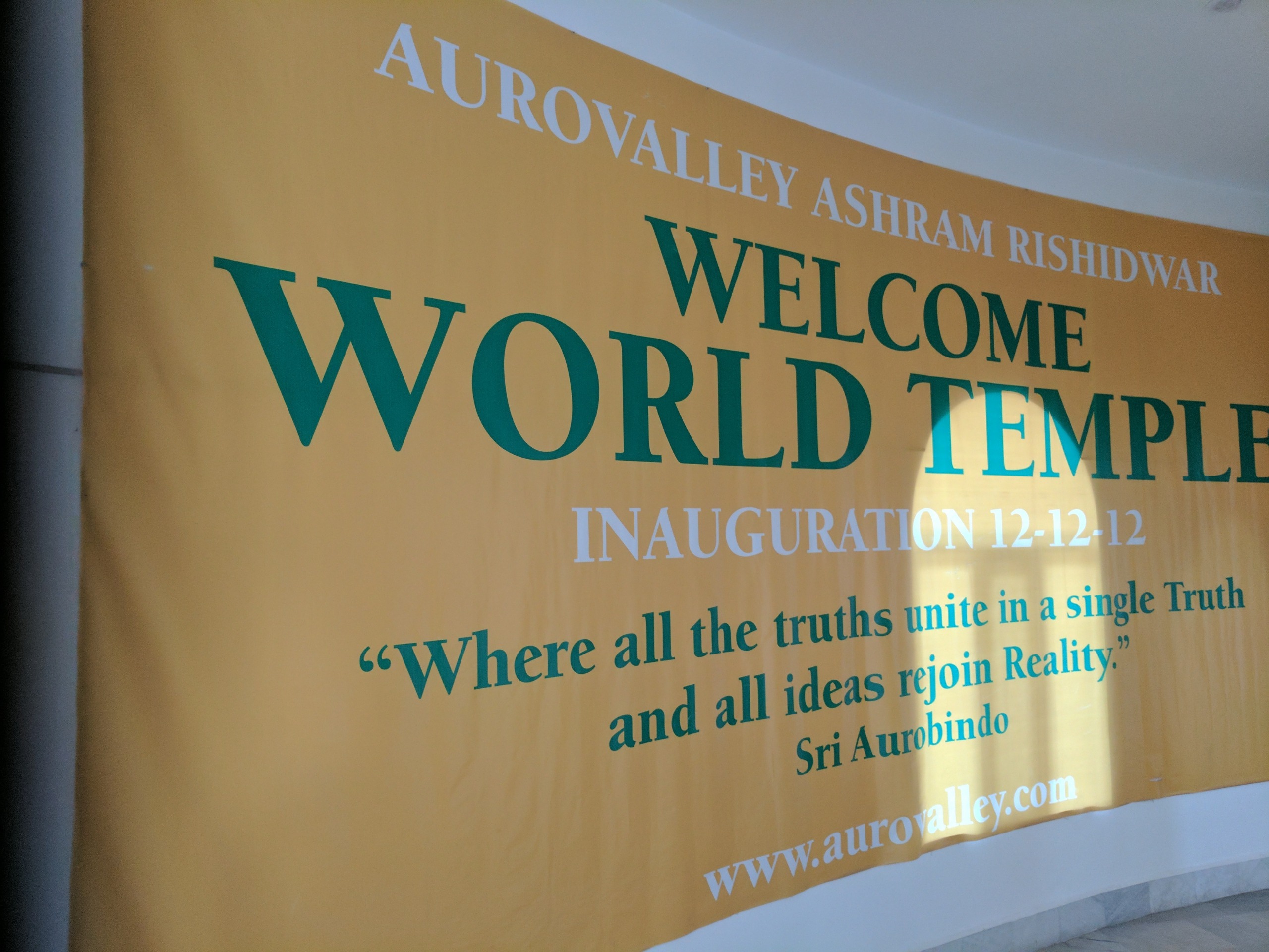 Welcome banner for Aurovalley Ashram's World Temple inauguration on 12-12-12, featuring a quote by Sri Aurobindo about unity of truths.