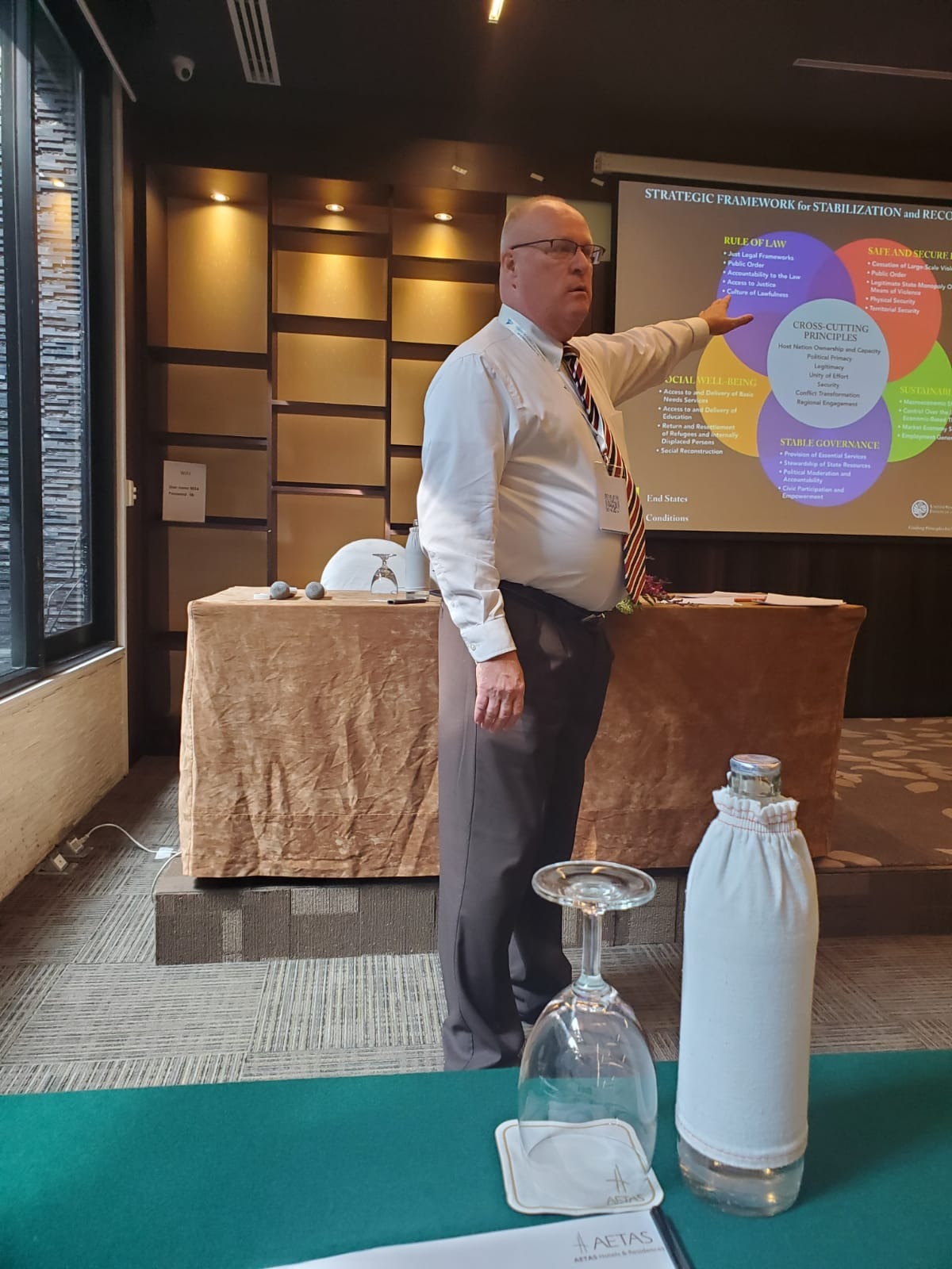 A presenter gestures toward a strategic framework display during a conference, illustrating key principles for stabilization and recovery.