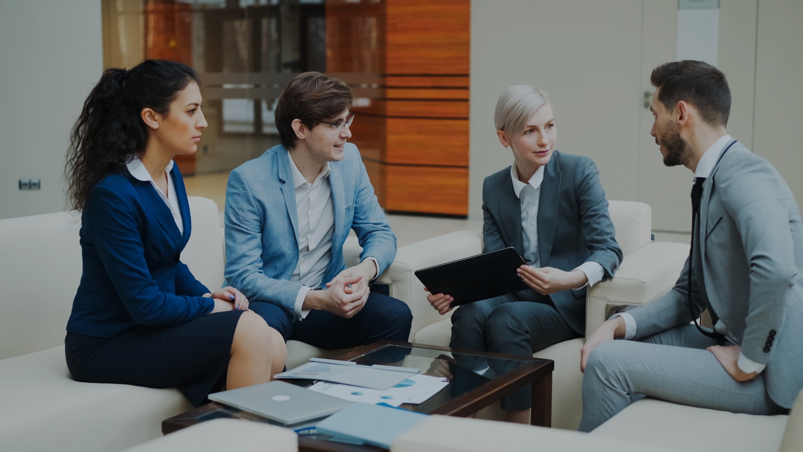 Business professionals engage in a collaborative discussion in a modern office setting, reviewing documents and strategies.