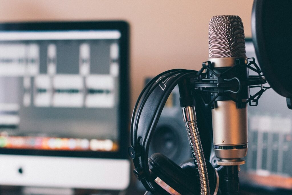 Microphone and headphones positioned near a computer screen displaying audio editing software, illustrating a recording studio setup.