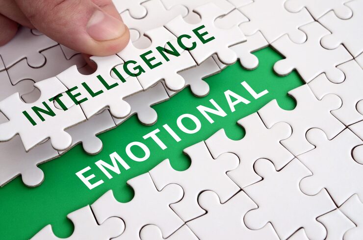 A hand places a puzzle piece labeled "INTELLIGENCE" into a partially completed puzzle. Below it, the word "EMOTIONAL" is visible, creating "EMOTIONAL INTELLIGENCE."