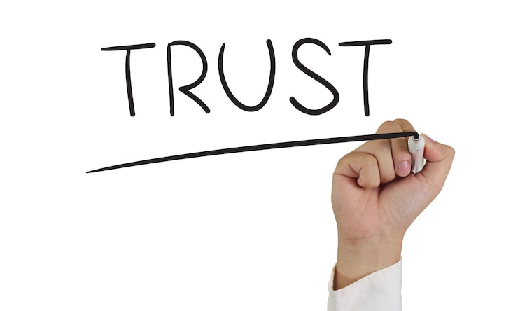 Hand holding a marker underlines the word "TRUST" written in black on a whiteboard. The image conveys confidence and reliability.