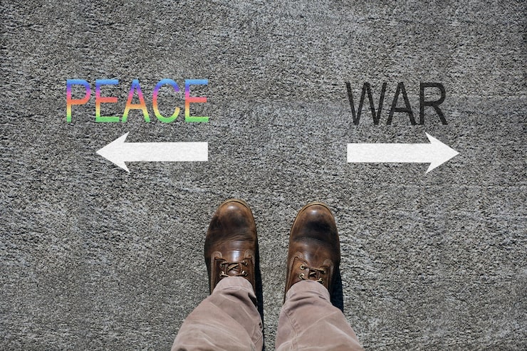 A person in brown shoes stands on gray pavement between two arrows. "Peace" in colorful letters points left; "War" in black points right, symbolizing choice.